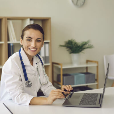 Woman doctor looking at camera during online meeting on laptop